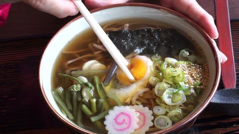 Hand eating Japanese soba noodle hot soup, using chopsticks to scramble raw egg yolk