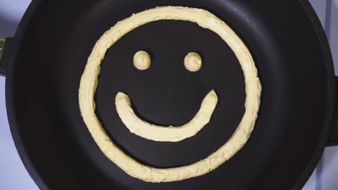 Smiley face made from butter, accelerated video. Butter being heated and melts in a skillet
