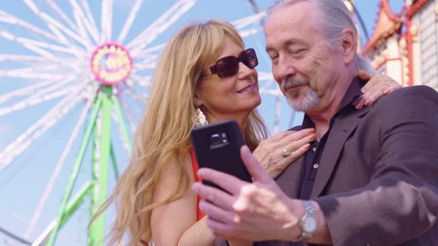 Older couple in love take self portrait on a mobile phone at an amusement park