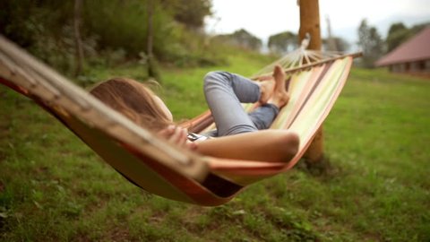 Young Caucasian female resting lying on hammock among two poles outdoors in slowmotion