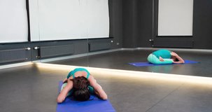 Woman doing yoga exercise in mirror studio 4k video. Fit athletic girl sitting on mat in asana posture: stretching in lotus position or padmasana