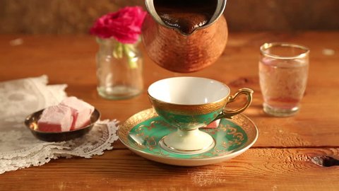 Pouring hot Turkish coffee in a traditional cup on a wooden table
