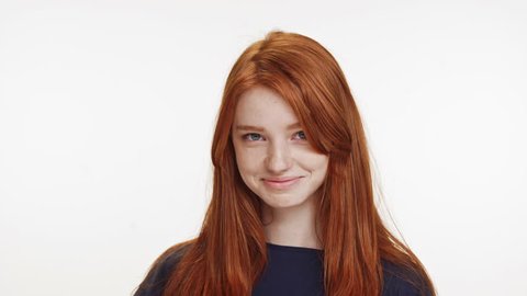 Shy coy ginger Caucasian teenage girl standing smiling on white background