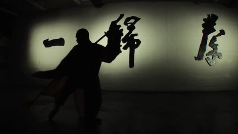 A Shaolin monk demonstrates in silhouette an ancient form of kung fu using a staff. Shot in slow motion. 