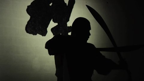 A Shaolin monk demonstrates in silhouette his ancient form of kung fu using two swords. Shot in slow motion. 