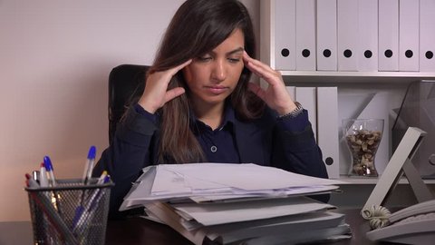 Stack paperwork exhausted businesswoman rubbing temples headache stressful job