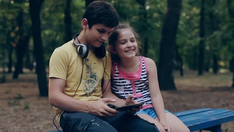 Children with tablet pc outdoors. Girl and boy on grass with computer