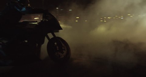 A man on a sport bike does serious burnouts / donuts in slow motion at night then drives off