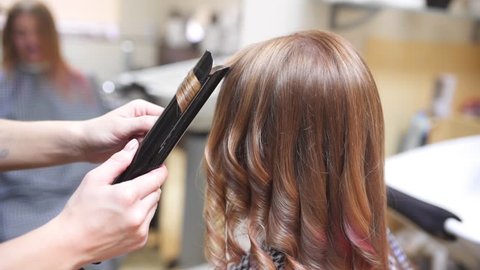 Barber makes curly hair for woman by hot curling, woman in the beauty studio, beauty and fashion business