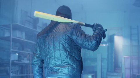 Masked bandit with baseball bat entering to the abandoned place. Shot on RED Cinema Camera in slow motion. 

