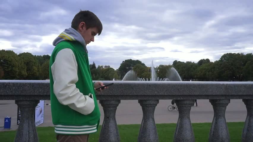 The man dials number on phone in the park in the cloudy fall