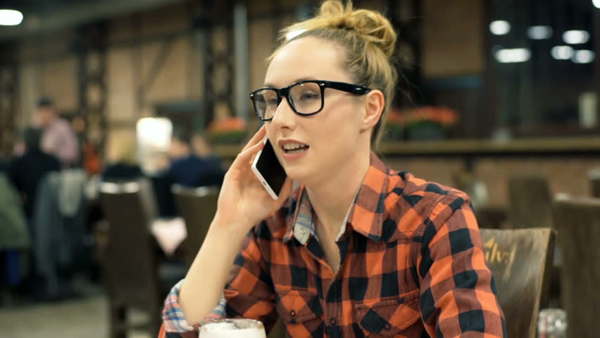 Happy girl in checked shirt sitting in the cafe and chatting on cellphone, steadycam shot

