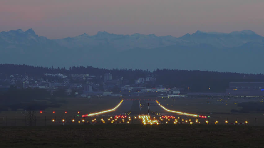 Airplane Landing At Zurich International Airport At Dusk With The Alps In Distant Background