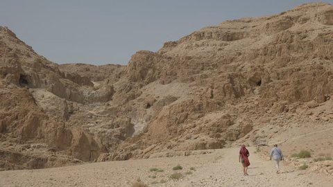 long shot of tourists walking towards the cave containing hills at qumran near the dead sea in israel