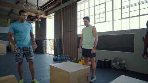 Instructor clapping his hands in encouragement while fit strong healthy people do box jumps in gym