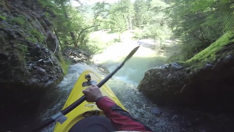 CLOSE UP: Extreme pro kayaker kayaking in raging whitewater river flowing over the edge of steep rocky mountain wall. Sportsman descending the rapids, paddling through the crack and running waterfall