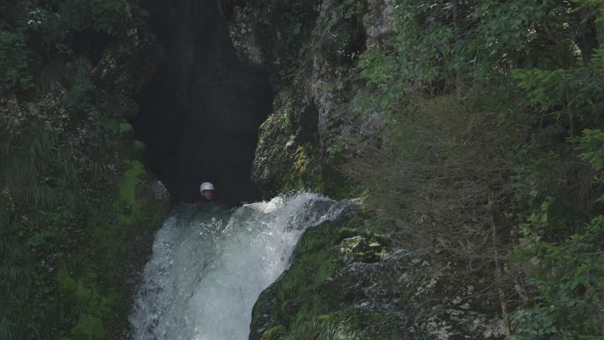 SLOW MOTION, CLOSE UP: Extreme pro canoer soaring above raging whitewater river washing rocky mountain ledge. Adrenaline rushing through man descending on the rapids and paddling through big waterfall Royalty-Free Stock Footage #23559721