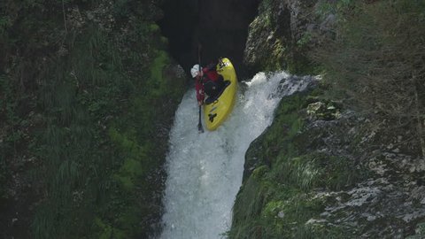 SLOW MOTION, CLOSE UP: Extreme pro canoer soaring above raging whitewater river washing rocky mountain ledge. Adrenaline rushing through man descending on the rapids and paddling through big waterfall