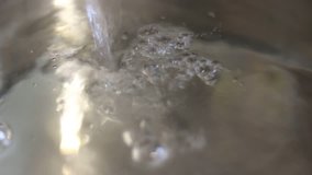 Clear transparent water flows to pan. Bubbles rise to surface in shiny metal pot