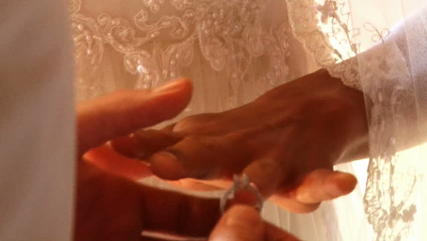 Groom places wedding ring on bride's finger during ceremony.