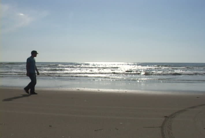 Man walks sandy, ocean shores in Oregon.