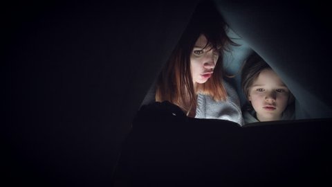 4k Shot of Child and Mom under Blanket Reading Horror Story Book