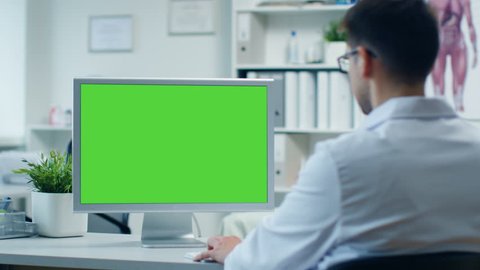 Doctor's Office. Male Doctor Works at His Personal Computer with Green Screen, His Assistant Comes in and Takes His Place at the Table. Modern Office. Shot on RED Cinema Camera 4K (UHD).