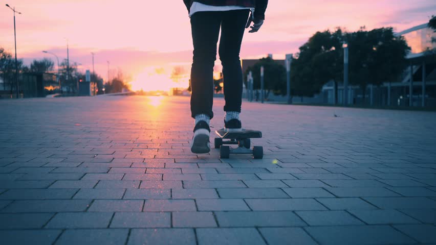 Beutiful and soft pink pastel lighning at winter time. Following camera with close up on skater legs, skating his longboard in city street into sunset Royalty-Free Stock Footage #23582566