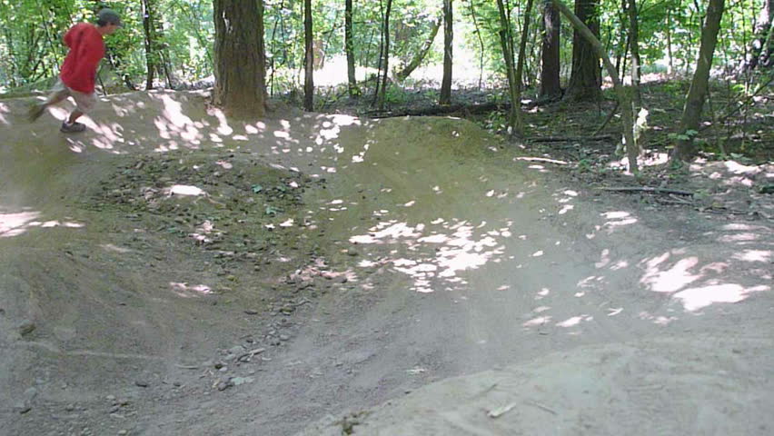 Man runs on dirt jumps as if he is a dirt bike in thick forest.