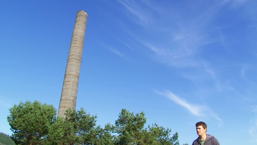 Man walking and passing by old, non working smoke stack outside on blue sky day.