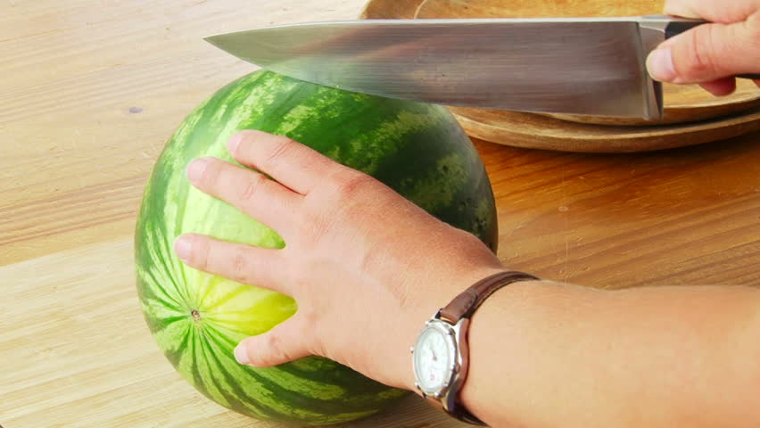 Woman cuts watermelon in half with knife.