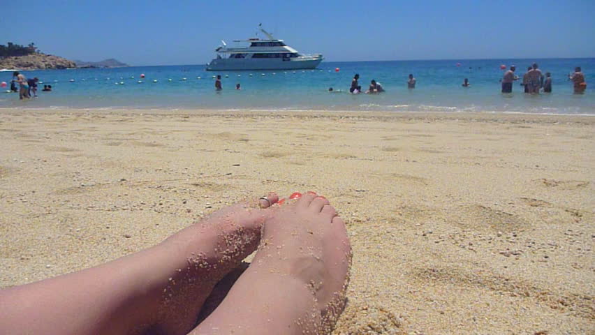 Woman's feet in sand with yacht in tropical location. Chileno Bay in Cabo,