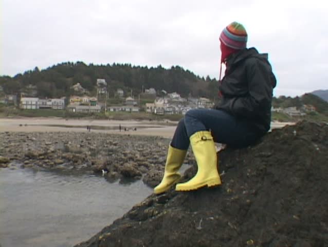 Woman at Haystack Rock in Cannon Beach, Oregon sits looking out by ocean. Series