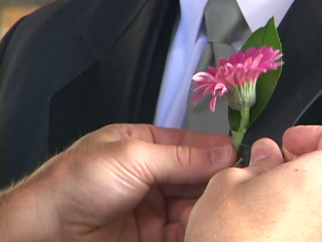 Groom gets help putting on boutonniere in preparations of wedding.