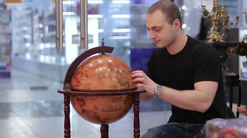 Young man examines a globe in a travel agency.