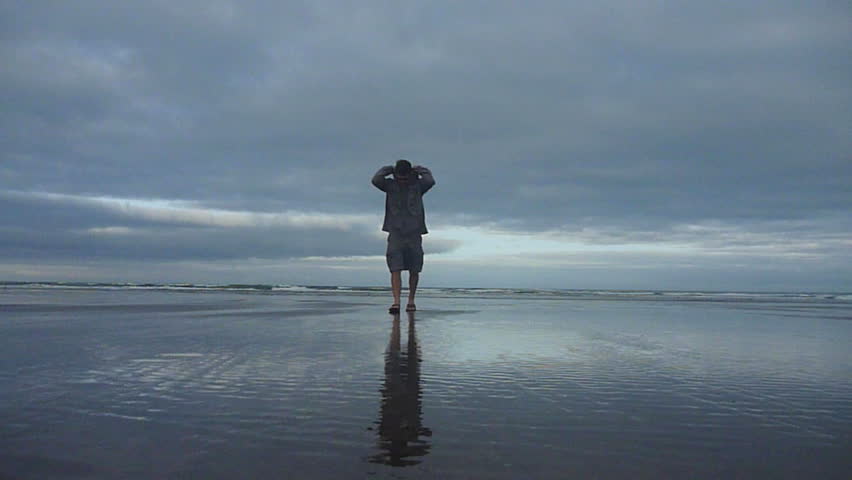 Man standing, then walks sandy beach away from Pacific Ocean in Oregon.
