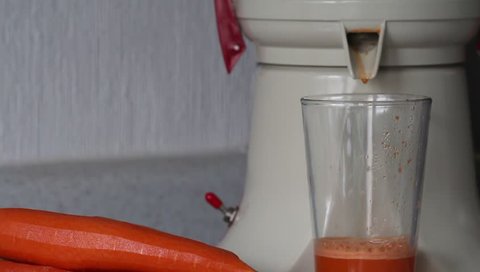 Fresh carrot juice pours of juicers in a glass on the table. Freshly squeezed juice for breakfast. A glass of vegetable juice with a juice extractor.