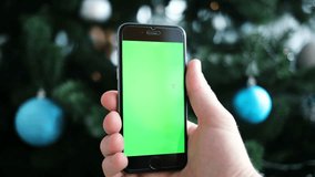 Green screen display phone at New Year night celebration in front of Christmas tree