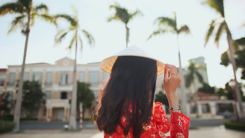 Vietnamese girl puts on a national cap Non La in the rays of the evening sunset in the city of Da Nang