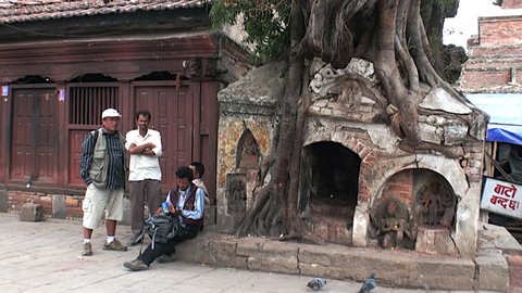Kathmandu, Nepal - 17 October 2011: Men sit near old tree with huge roots on Durbar Square. General plan.