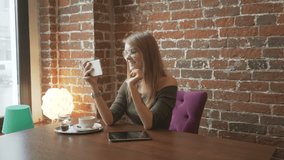 Young smiling woman having video conversation using smartphone in coffee shop,