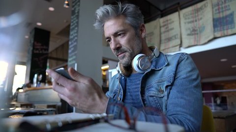 Mature guy with eyeglasses connected on smartphone in bar