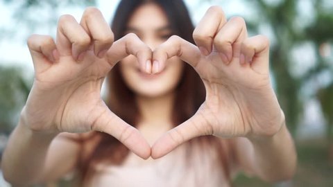 Slow motion : Young woman making heart shape by her hand and smiling
