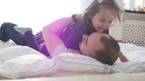 Happy Family Idyll Father Hug Little Child Daughter Playfully Roll Over A Bed At Home