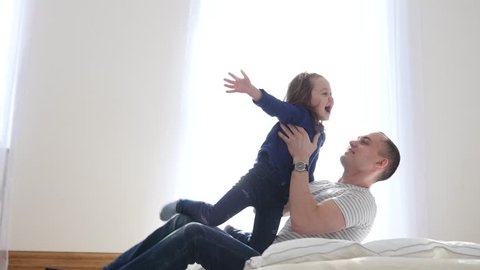 Little Child Girl Daughter Have Fun Jump To Father Arms So They Falling On A Bed