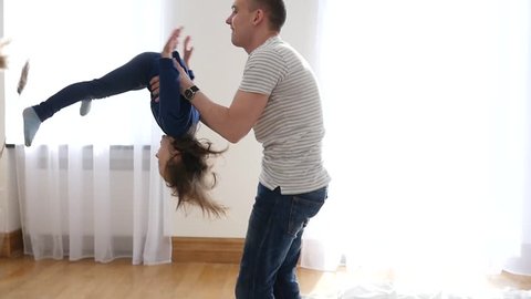 Happy Family At Home Father Entertain Little Child Daughter Throw And Spin Her In Air And Then They Falling On A Bed