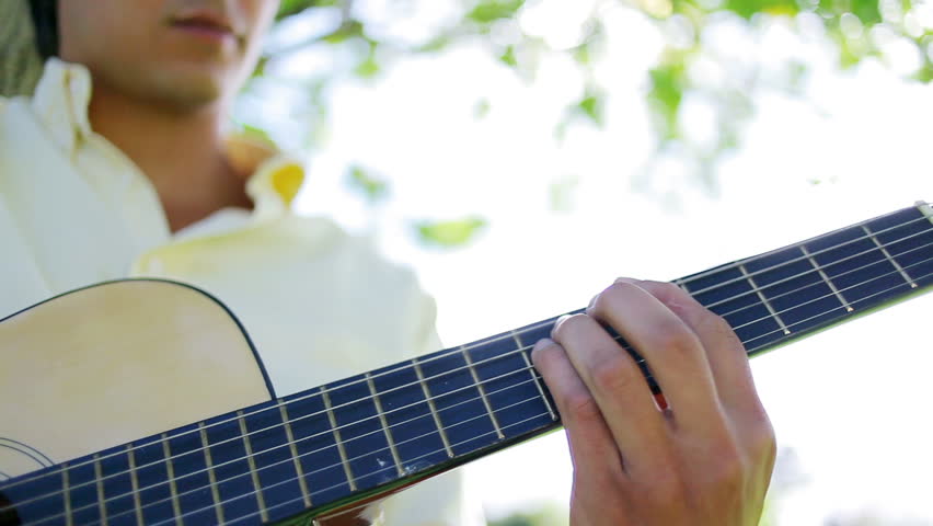 Serious man playing music with his acoustic guitar in the countryside