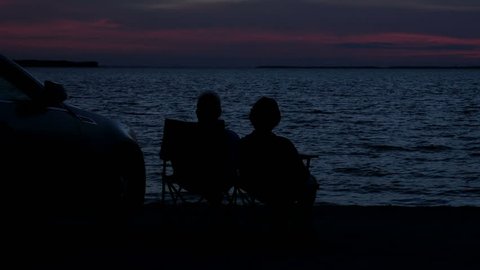 Silhouettes of a couple sitting at the beach watching the ocean at twilight