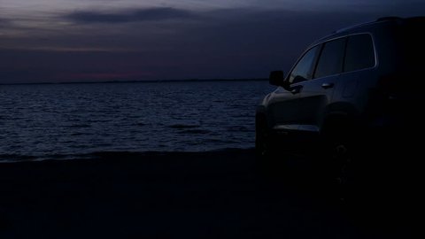 Silhouette of a SUV car at the beach with oceanview at twilight after sunset with some red clouds
