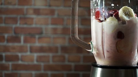 Blender with a banana strawberry milk smoothie on the kitchen, slow motion
